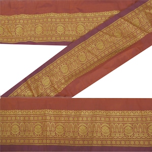 May include: A length of fabric in shades of rust and purple, with a gold decorative border. The border features a repeating floral pattern. The fabric is folded and arranged diagonally across the frame, showcasing the design.