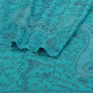 May include: Teal blue fabric with a delicate floral embroidery pattern. The fabric is sheer and has a soft, flowing texture.