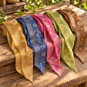 May include: A collection of five long, rectangular scarves in mustard yellow, royal blue, hot pink, lime green, and copper brown. Each scarf features a repeating floral pattern with intricate metallic-toned borders and a delicate, woven texture.