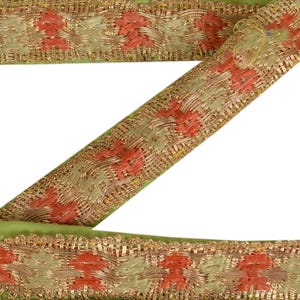May include: Close-up of decorative trim with a repeating pattern. The trim features a light green base with a woven design in gold, peach, and cream colors. The trim is likely used for embellishing clothing or craft projects.