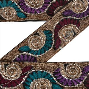 May include: Decorative embroidered trim featuring a repeating pattern of teal, purple, and burgundy leaves with silver sequins. The trim has a gold metallic border and a black background. This trim is suitable for various craft projects.