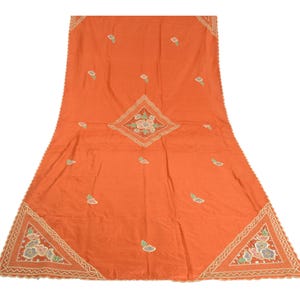 May include: A rectangular orange fabric piece featuring a central diamond-shaped floral embroidery and matching triangular floral patterns at the bottom corners. The edges are finished with a scalloped border and intricate white stitching.