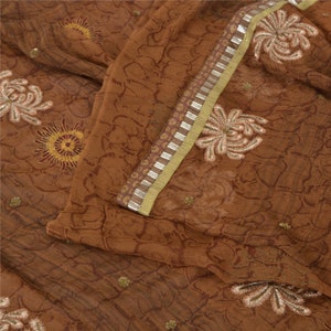 May include: Brown fabric with a floral pattern and a gold and silver trim. The fabric has a textured surface and is decorated with embroidered flowers.