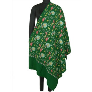 May include: A green shawl with floral embroidery. The shawl features a detailed pattern of flowers in shades of blue, yellow, and pink, with green leaves and vines. The border is a darker green with embroidered details. The shawl is draped over a black mannequin.