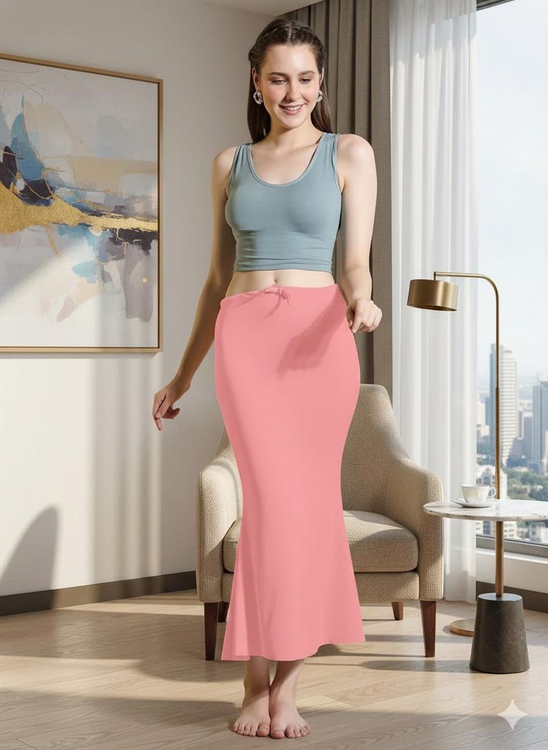 May include: A light blue tank top paired with a coral pink skirt. The skirt has a drawstring waist and a fitted silhouette that flares out at the hem. The outfit is simple and elegant.