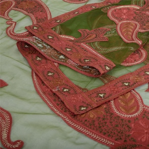 May include: A green sheer fabric with intricate embroidery in shades of pink and gold. The fabric has a delicate, lacy texture and features a floral design.