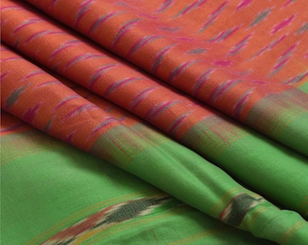 May include: Close-up of a folded fabric with a vibrant color palette. The top layer features an orange hue with pink and gray accents, while the bottom layer is a bright green. The fabric appears to be silk or a similar material, with a soft, flowing texture.