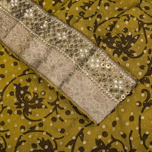 May include: An olive green fabric featuring a dark brown floral pattern and scattered gold metallic dots. A wide, decorative border runs diagonally across the material, embellished with rows of gold sequins and intricate metallic embroidery.