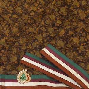 May include: A brown sheer fabric with a floral print and a green, white, and brown border. The fabric has a decorative embellishment in the lower left corner.