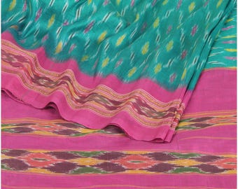 May include: A vibrant textile featuring a teal background with a repeating pattern of yellow and pink shapes. The fabric has a bright pink border with intricate designs in brown, yellow, and pink. The textile is folded, showcasing its texture and color variations.