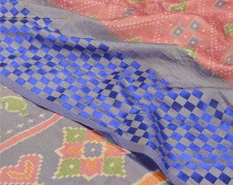 May include: Close-up of a patterned textile with a blue checkered border. The fabric features a mix of pink, gray, and blue hues with geometric designs. The textile has a soft, flowing appearance, suggesting a lightweight material.