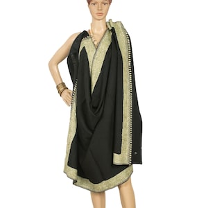 May include: A black shawl with a gold embroidered border and accents is draped over a mannequin. The shawl is made of a soft fabric and has a detailed pattern along the edges. The mannequin is wearing gold bangles and a necklace.