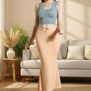 May include: A woman wearing a light blue crop top and a peach-colored, floor-length skirt. The skirt has a slight flare at the bottom. The outfit is simple and elegant, suitable for casual or semi-formal occasions.