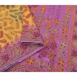 May include: A colourful textile with detailed embroidery. The fabric showcases yellow and purple tones, with intricate floral and leaf patterns in orange, red, and black. The design includes a decorative border.