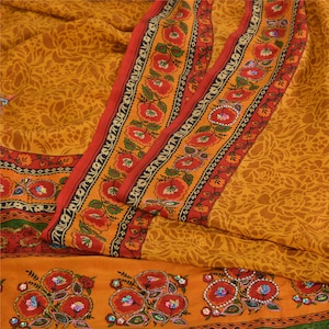May include: A mustard yellow fabric featuring a tonal floral pattern with a wide border. The border displays a repeating red floral motif with green leaves and black accents. The lower section includes embroidered red flowers with sequins.