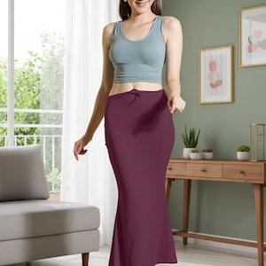 May include: A woman wearing a light blue tank top and a burgundy-colored skirt. The skirt is a fitted, floor-length style with a slight flare at the bottom. The outfit is simple and elegant, suitable for various occasions.