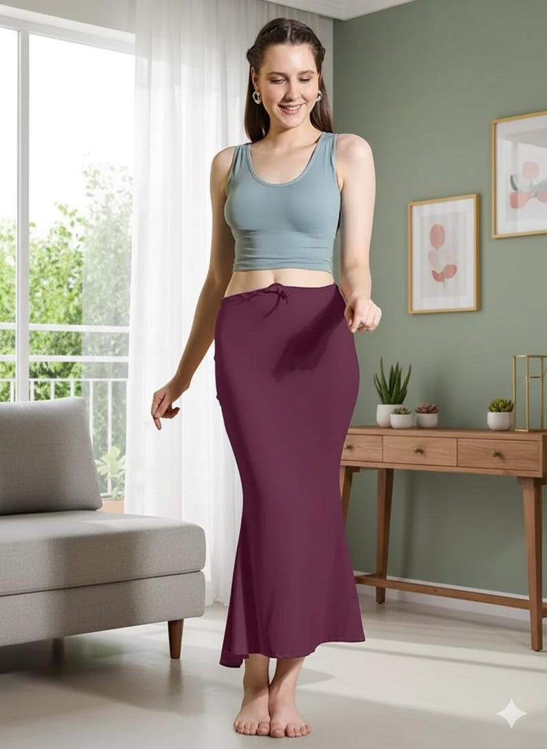 May include: A woman wearing a light blue tank top and a burgundy-colored skirt. The skirt is a fitted, floor-length style with a slight flare at the bottom. The outfit is simple and elegant, suitable for various occasions.