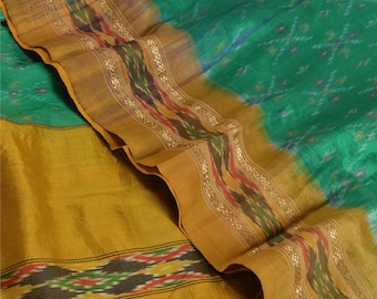 May include: A close-up of a silk textile with a vibrant color palette. The fabric features a combination of green and golden-yellow hues, with a decorative border in shades of brown, red, and gold. The textile has a textured appearance and a subtle sheen.
