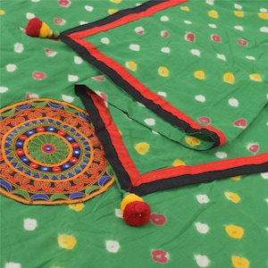 Può includere: Tessuto verde con pois bianchi, gialli e rosa. Il tessuto ha un bordo nero e rosso ed è decorato con nappe colorate. È presente anche un disegno circolare ricamato con dettagli arancioni, blu e verdi.