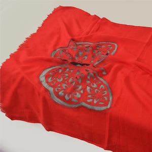 May include: A red scarf with a large, cut-out butterfly design. The butterfly is a light gray color and has intricate details.