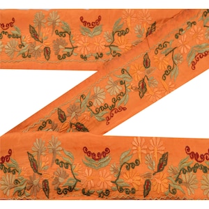 以下が含まれることがあります： オレンジ色の刺繍入り生地トリム。緑、黄色、赤の色合いの花と葉のデザイン。トリムは、花とつるの繰り返し模様が特徴で、衣類や家の装飾プロジェクトに装飾的なタッチを加えるのに最適です。