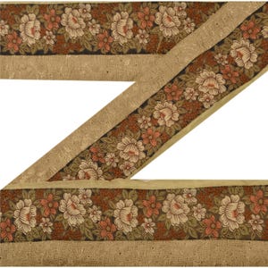 May include: A brown and beige floral trim with a repeating pattern of white flowers and green leaves. The trim has a gold metallic thread running through it.
