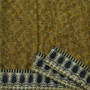 May include: A folded fabric with a floral pattern in shades of olive green and brown. The border features a repeating design of dark blue teardrop shapes and gold diamond accents on a cream background.