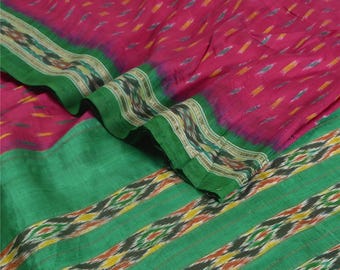 May include: A vibrant textile featuring a pink background with a pattern of small, colorful dashes. The fabric is bordered by a wide green stripe with a decorative band of black, yellow, and orange. The textile is folded, showing its texture.