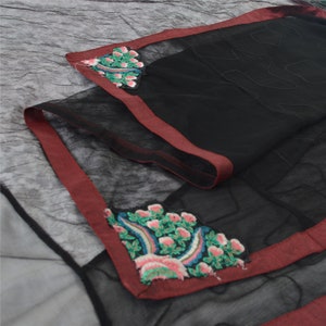 May include: A black sheer fabric scarf featuring a dark red border and intricate floral embroidery in shades of pink, green, and blue at the corners. The scarf has a subtle, wavy stitched pattern throughout the black mesh material.