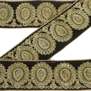 May include: Black velvet ribbon with gold embroidered floral and teardrop designs. The ribbon features intricate detailing with a metallic sheen, suitable for embellishments and crafts.