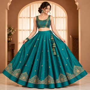 Könnte beinhalten: Ein blaugrünes Lehenga-Choli-Set bestehend aus einer ärmellosen Bluse und einem bodenlangen Rock. Der Rock ist mit goldenen Stickmustern am Saum und verstreuten Motiven verziert, ergänzt durch ein dekoratives Quastenband an der Taille.