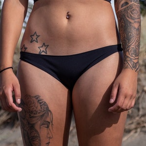 May include: A woman wearing a black bikini bottom with a star tattoo on her hip and a floral tattoo on her thigh.