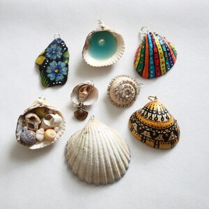 May include: Assortment of seven seashell pendants, each with a unique design. Some shells are painted with colourful patterns, while others are decorated with beads and glitter. The shells are all strung on silver chains and ready to be worn as necklaces.