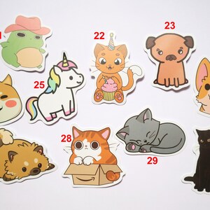 May include: A set of ten colorful cartoon animal stickers. The stickers feature a frog wearing a cowboy hat, a unicorn, a cat with a birthday hat, a pug, a corgi, a Shiba Inu, a cat in a box, a sleeping cat, a black cat, and a fluffy dog.