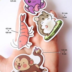 May include: Four different sized stickers featuring cartoon animals and objects. The stickers are on a hand. The stickers are: a purple octopus, a red shrimp, a brown hamster on a green watermelon slice, and a brown monkey holding a boba tea.