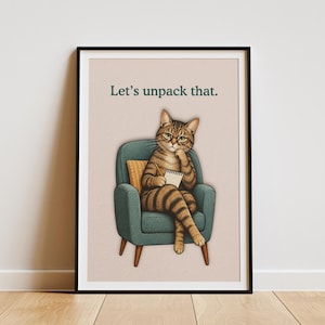 May include: A framed wall art print featuring a brown tabby cat with glasses sitting in a teal armchair, holding a notepad and pencil. The cat has one paw to its chin in a thoughtful pose. The text "Let's unpack that." is printed in dark green.