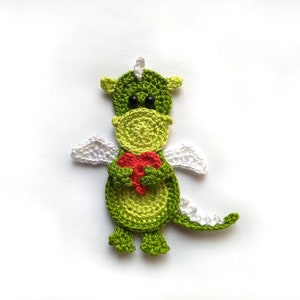 Pode incluir: Um dragão de crochê feito à mão em tons de verde, segurando um coração vermelho. O dragão tem asas brancas e olhos pretos. Este item é ideal para um berçário ou como um presente único.