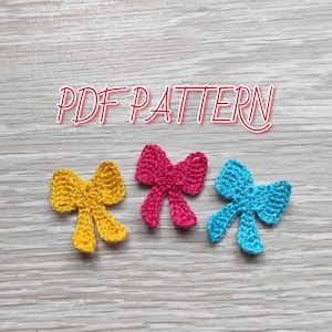 May include: Three crocheted bows in different colors: yellow, pink, and blue. The bows are on a wooden surface with the text "PDF PATTERN" above them.