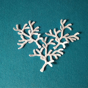 May include: A white crocheted snowflake design with three branches, on a teal blue background.