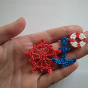 May include: A set of three crocheted nautical themed ornaments. The ornaments are a red and white life preserver, a blue anchor, and a red ship's wheel.