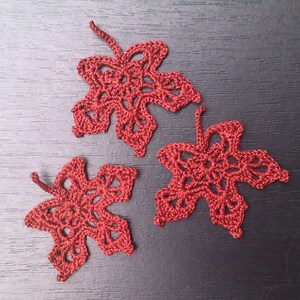 May include: Three handmade, crocheted maple leaves in a deep red hue. The leaves are intricately designed with openwork patterns, showcasing the delicate texture of the yarn. Perfect for fall-themed crafts and decorations.