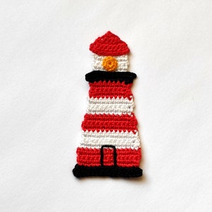 Puede incluir: Un faro hecho a mano con ganchillo en rojo, blanco y negro. El faro presenta rayas horizontales rojas y blancas, un tejado rojo y una base negra. Un pequeño círculo amarillo está en la parte superior. Sobre un fondo blanco.