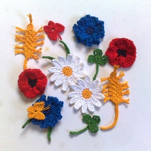 Pode incluir: Uma coleção de flores e folhas de crochê coloridas. O arranjo inclui papoulas vermelhas, margaridas azuis e brancas, flores amarelas pontiagudas, flores azuis com borboletas amarelas e trevos verdes. Os elementos florais feitos à mão estão espalhados em uma superfície branca.
