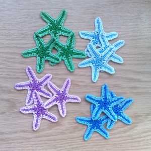May include: A set of crocheted starfish in various shades of green, blue, and purple. The starfish are arranged in a cluster on a wooden surface.