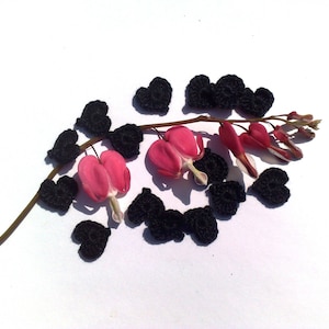 Può includere: Un delicato fiore rosa con decorazioni a forma di cuore in crochet nero su uno sfondo bianco.