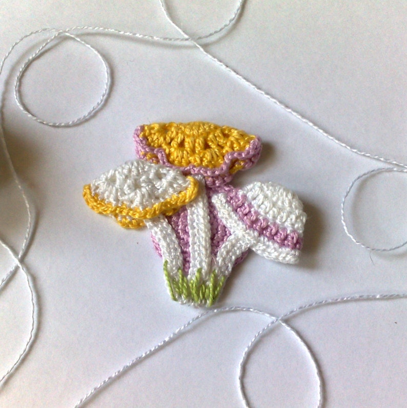 Puede incluir: Una aplicaci&oacute;n de flores de ganchillo hecha a mano con detalles en amarillo, blanco, rosa y verde. La flor tiene un dise&ntilde;o detallado con m&uacute;ltiples capas y est&aacute; hecha con hilo. Hilo blanco en el fondo.
