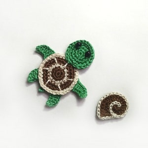May include: Crocheted turtle and seashell appliqués. The turtle has a green head and limbs, a brown and cream shell, and black eyes. The seashell is brown and cream. These are likely for crafting or embellishment.