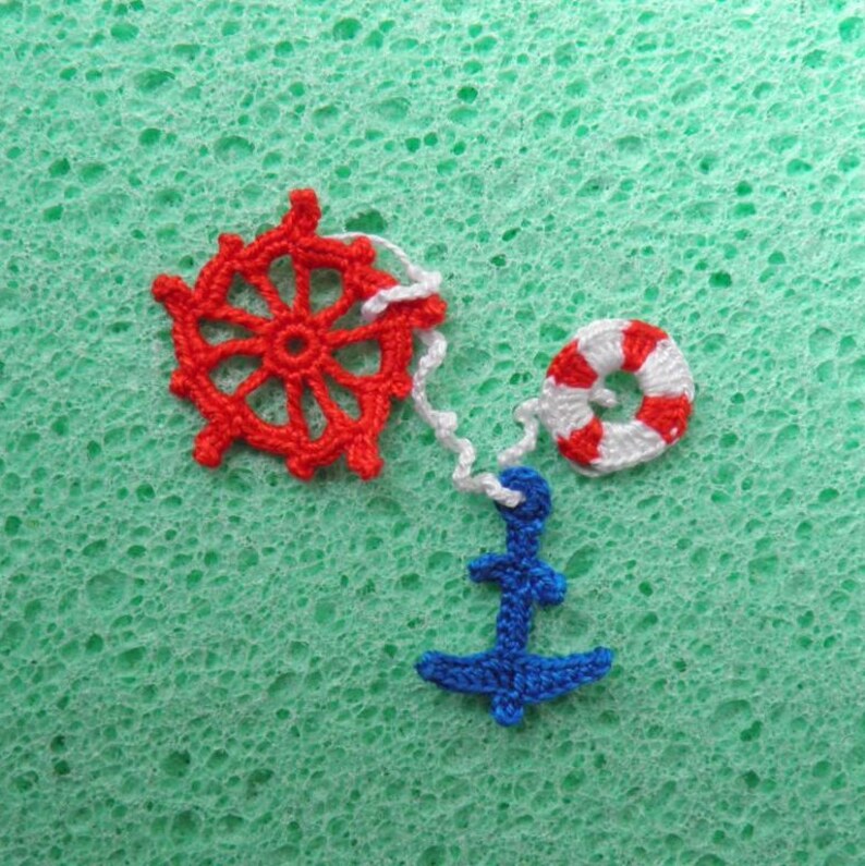 May include: A red and white crocheted nautical themed charm set with a wheel, life preserver, and anchor.