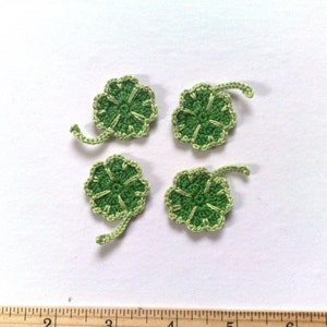 Peut inclure: Quatre trèfles à quatre feuilles crochetés à la main. Chaque trèfle est vert vif avec une bordure et une tige vert clair. Les trèfles sont disposés sur une surface blanche, mettant en valeur le savoir-faire détaillé du crochet.