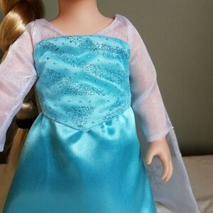 May include: A blue and white dress with a sparkly bodice and sheer sleeves. The dress is made of satin and has a princess-like silhouette.